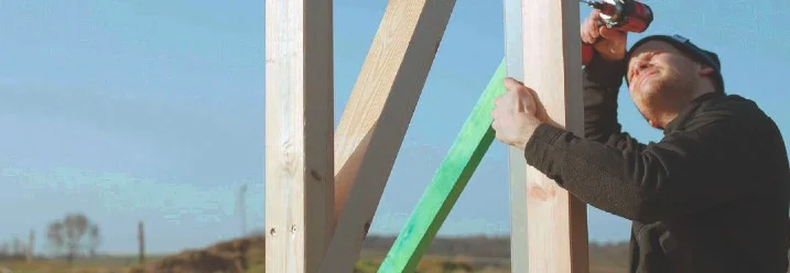 Person schraubt Holzbalken an einer Konstruktion fest.